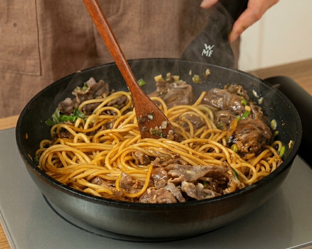 Tossing and stirring spaghetti, beef, and a dark sauce together in a pan with a wooden spatula.