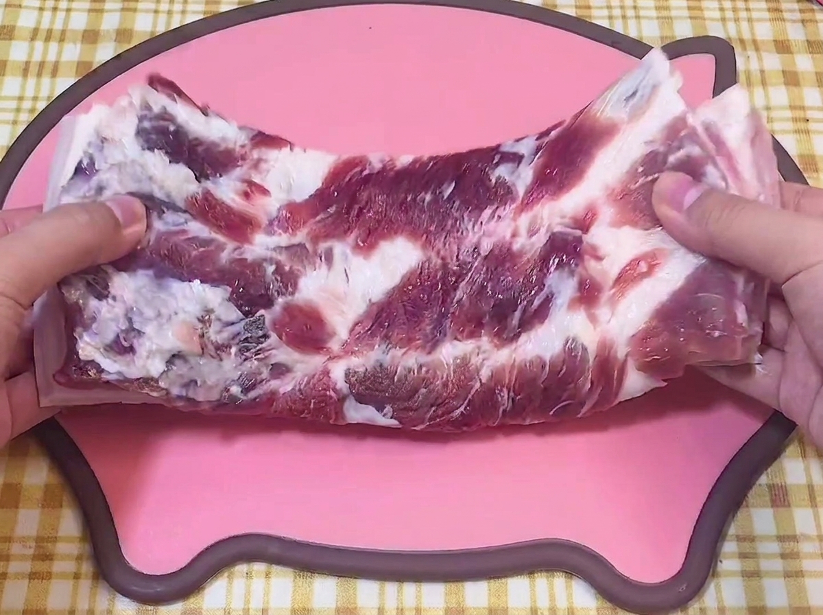 Hands holding a slab of raw pork belly on a pink pig-shaped cutting board.