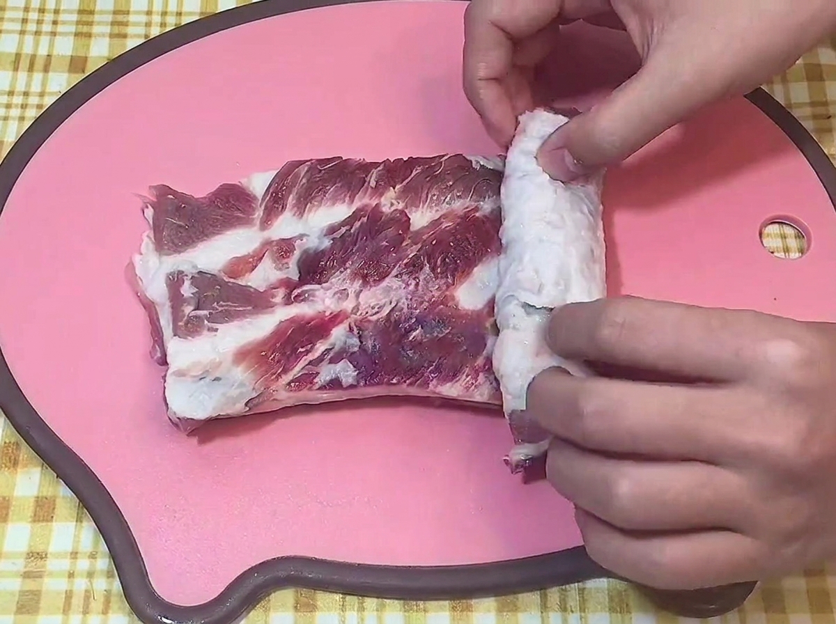 Hands rolling a scored piece of raw pork belly into a tight log on a cutting board.