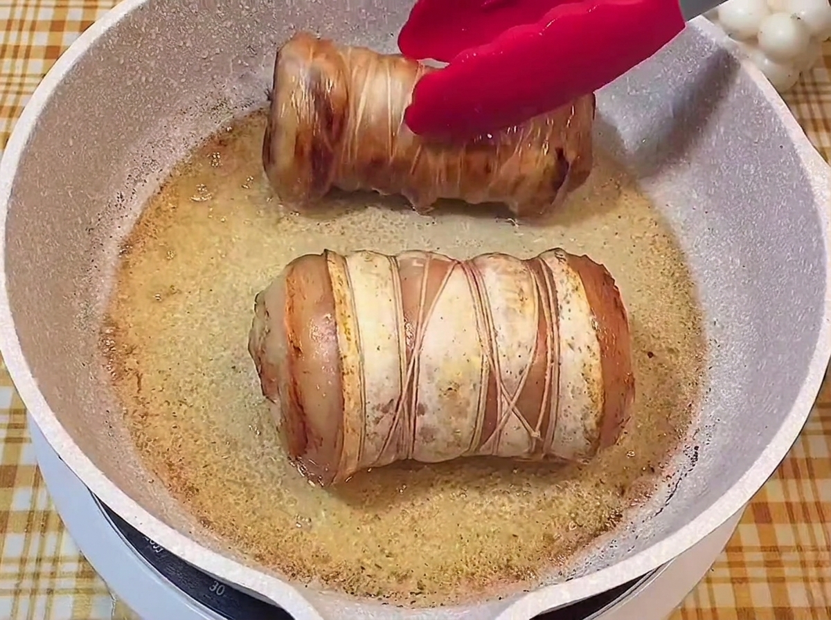 Two tied pork rolls with a beautifully browned, crispy exterior sizzling in a frying pan.