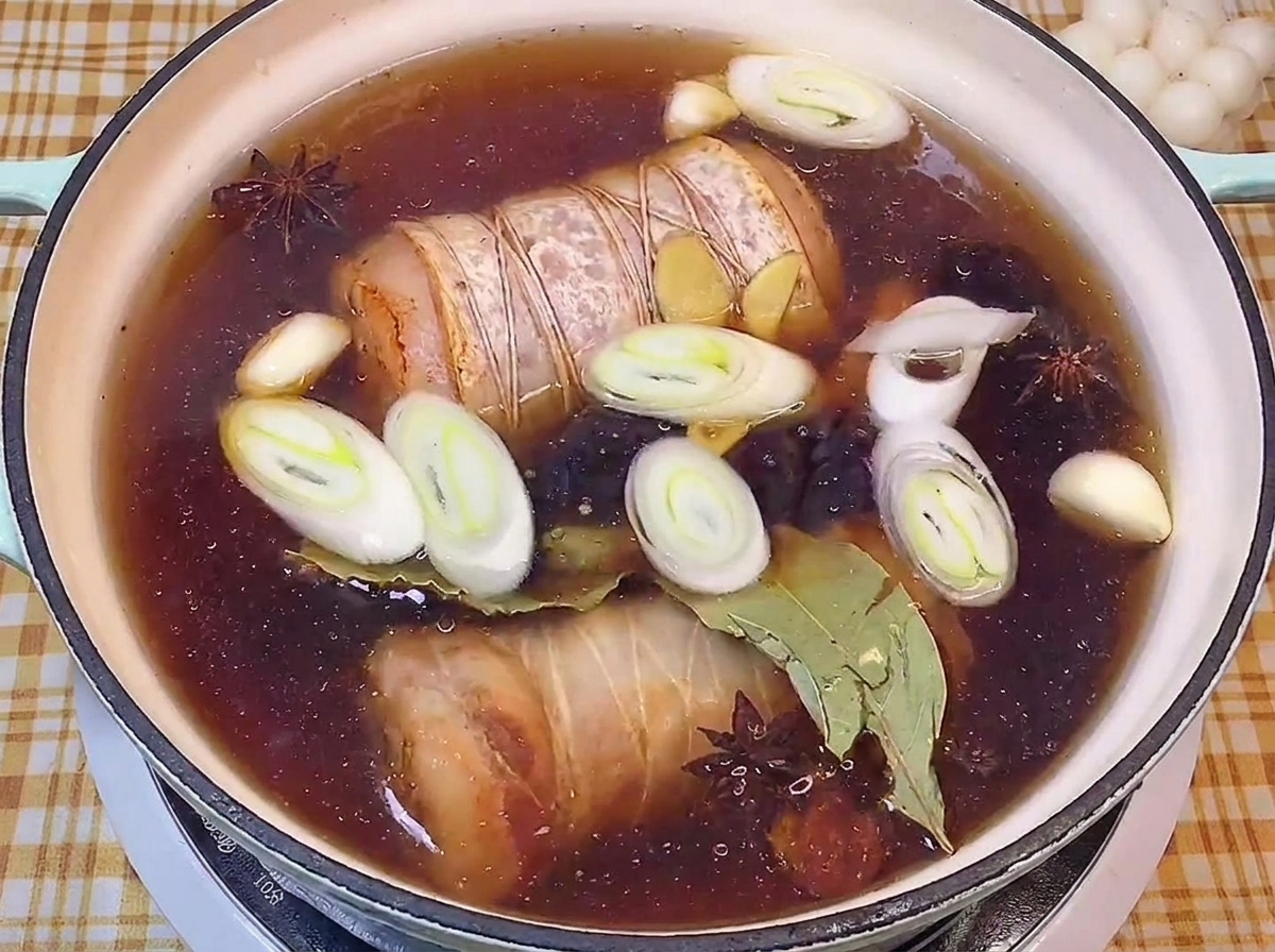 Rolled pork belly secured with butchers twine simmering in a dark soy sauce broth with leeks, garlic, and star anise.