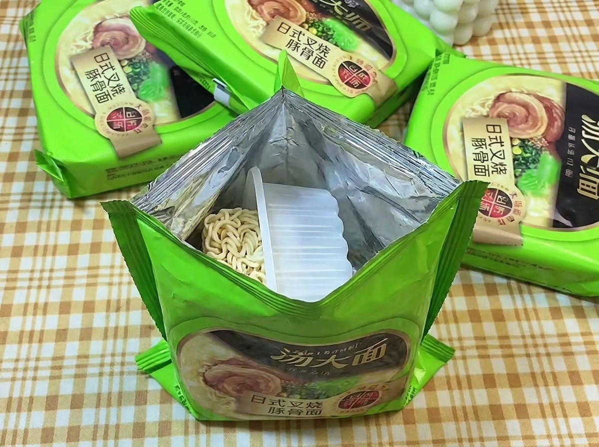 An opened green package of instant ramen exposing the dry, wavy noodle block sitting in a clear plastic tray.