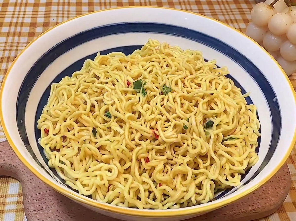 Cooked wavy ramen noodles neatly folded and arranged in the center of a blue and white rimmed ceramic serving bowl.
