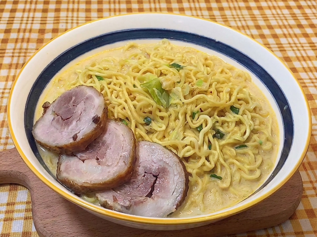 Three slices of rolled braised pork chashu placed over ramen noodles in a creamy broth.