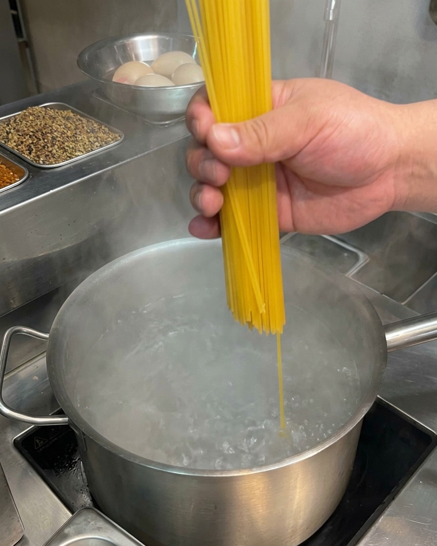 A hand placing dry spaghetti into a pot of rapidly boiling water.