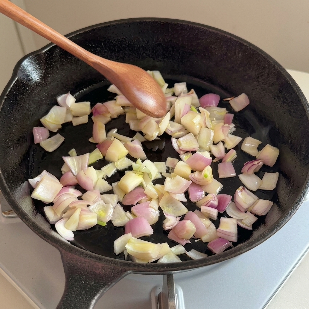 Chopped onions being sautéed in a cast-iron skillet with a wooden spoon.