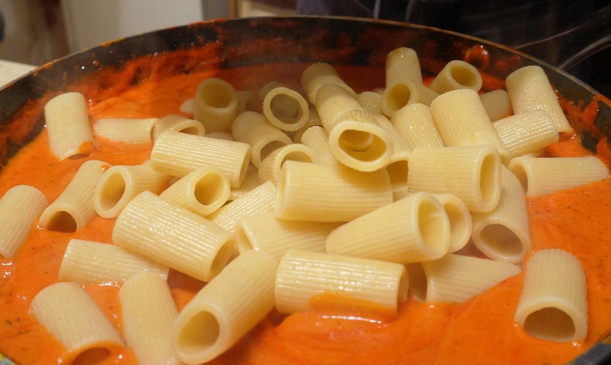 Adding cooked rigatoni pasta into a skillet filled with a smooth, creamy orange-red sauce.