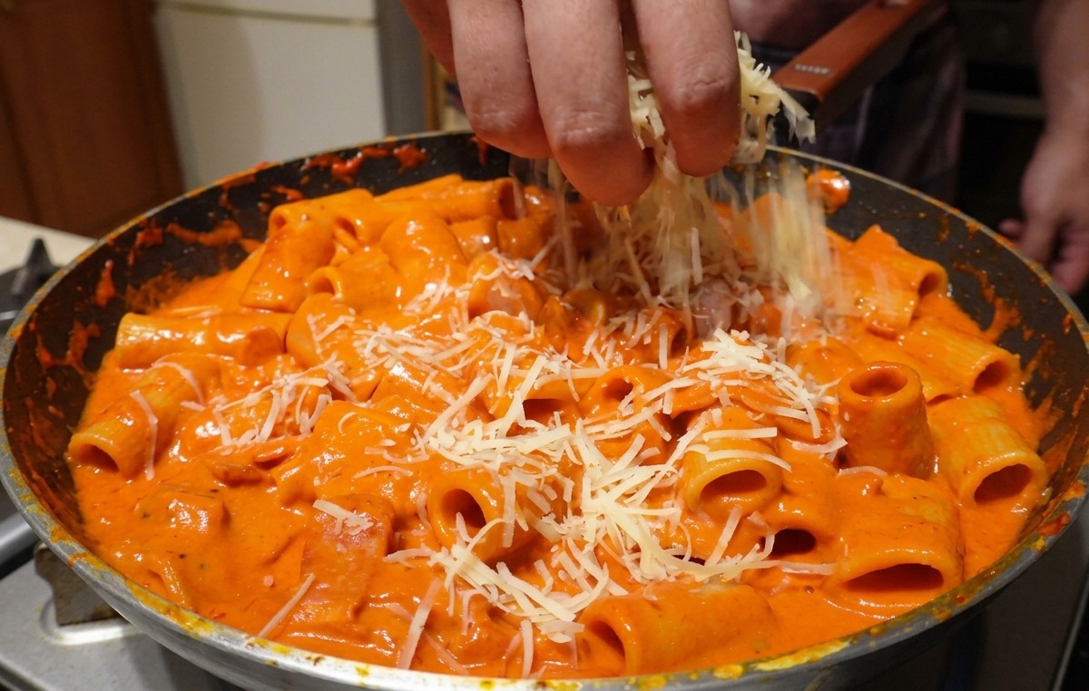 Grated parmesan cheese being generously sprinkled by hand over large rigatoni pasta mixed in a creamy pink vodka sauce.