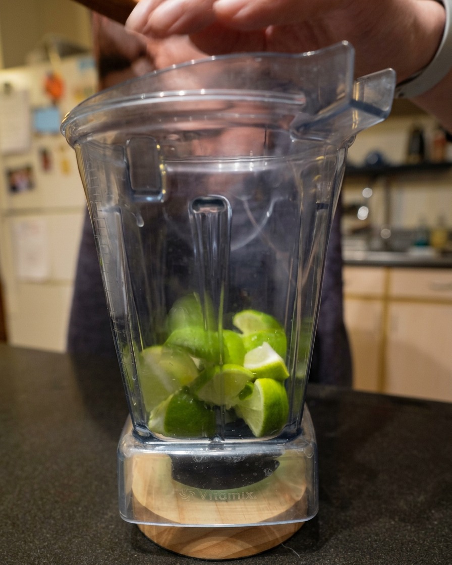 Fresh chopped lime wedges inside a clear Vitamix blender pitcher.