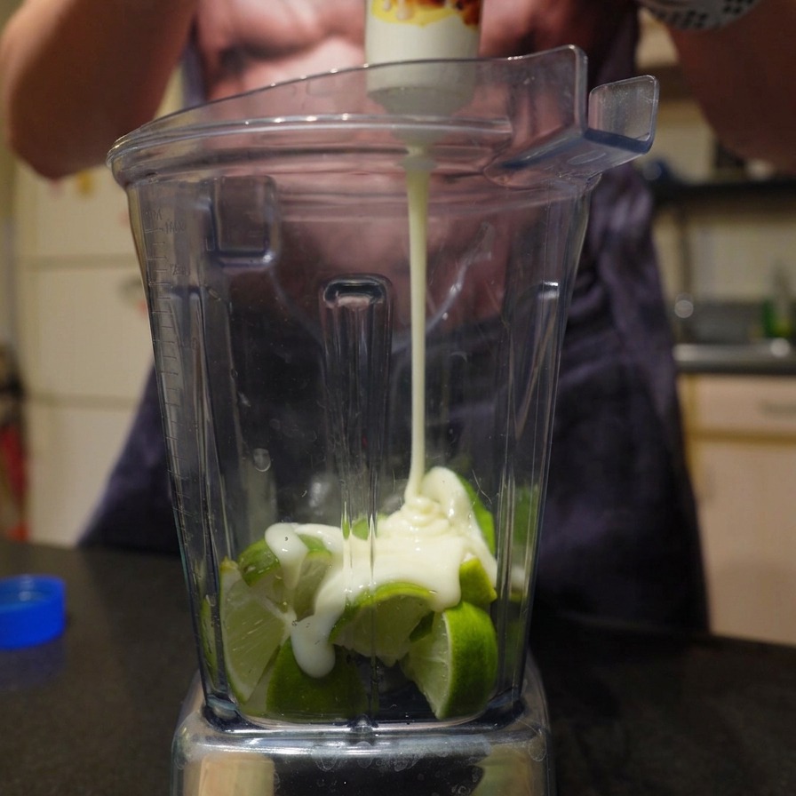 Squeezing thick sweetened condensed milk from a tube over fresh chopped limes in a blender.
