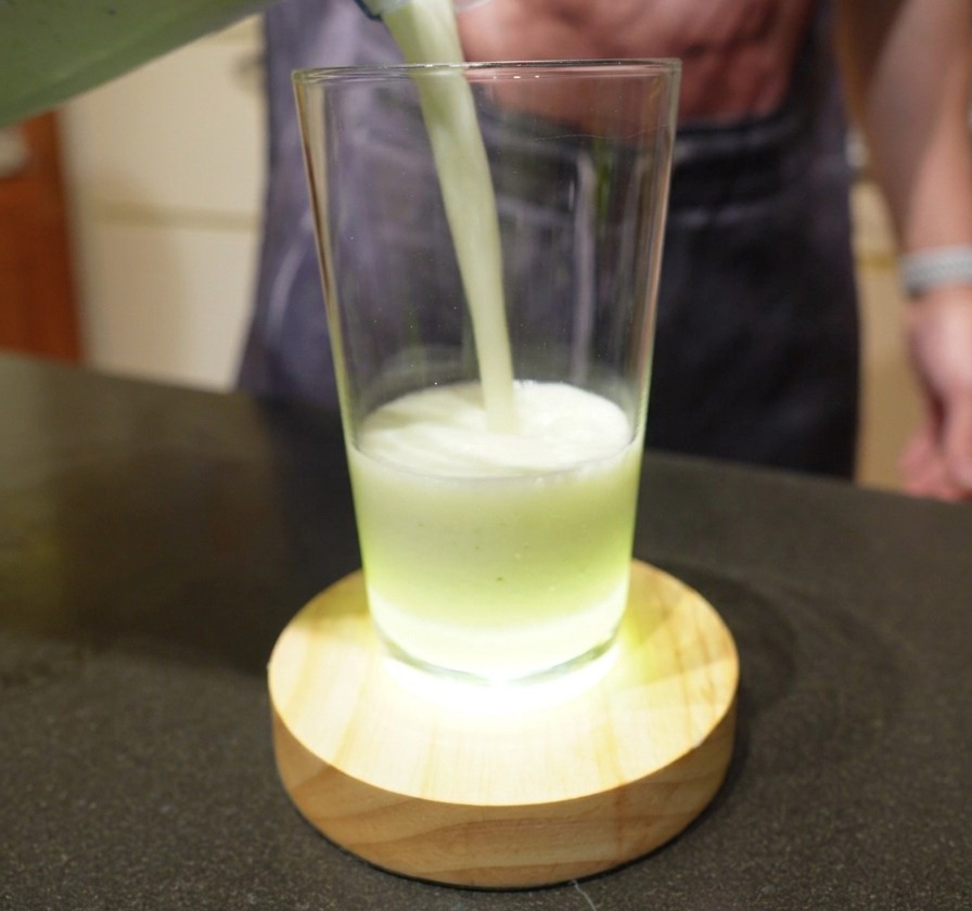 Pouring a creamy, pale green blended lime drink from a blender into a clear glass.