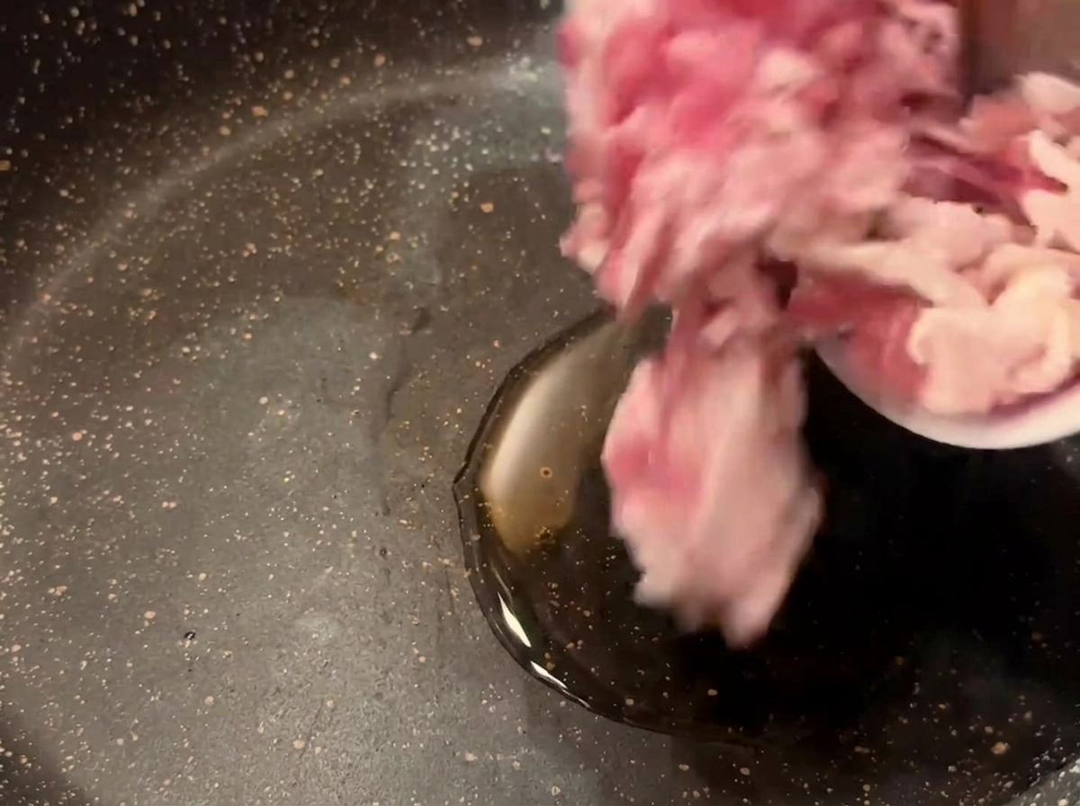 Chopped raw bacon pieces being poured from a small bowl into a dark skillet with heated cooking oil.