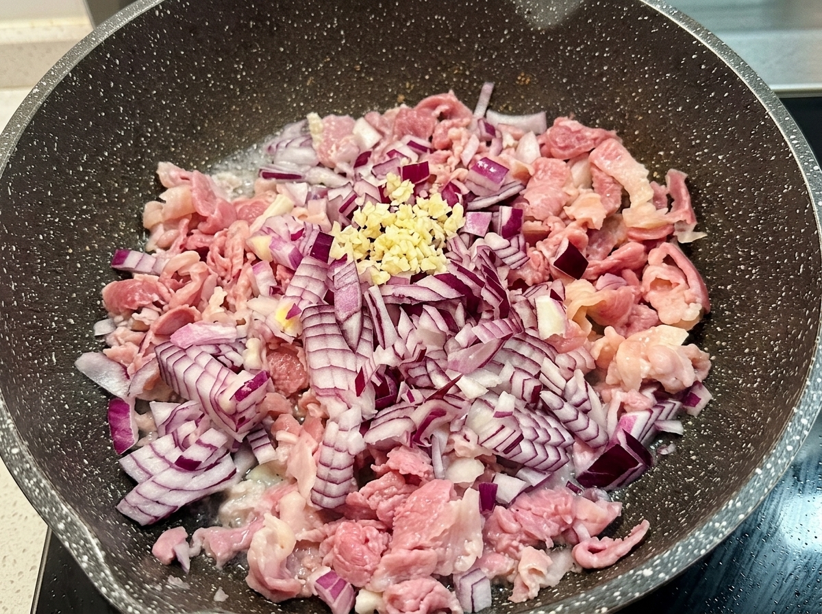 A small pile of fresh minced garlic sitting on top of sautéed chopped red onion and bacon in a cooking pan.