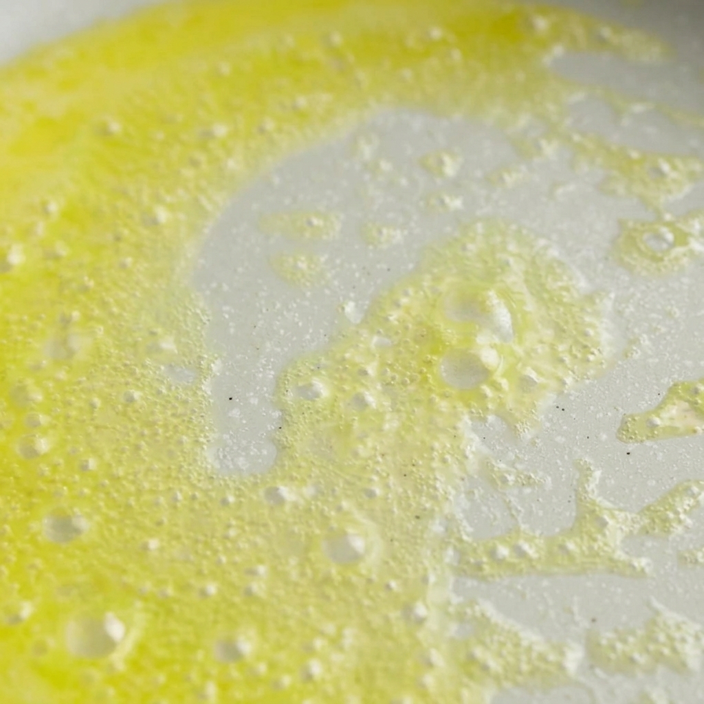 Yellow butter melting and bubbling in a light-colored frying pan over heat.