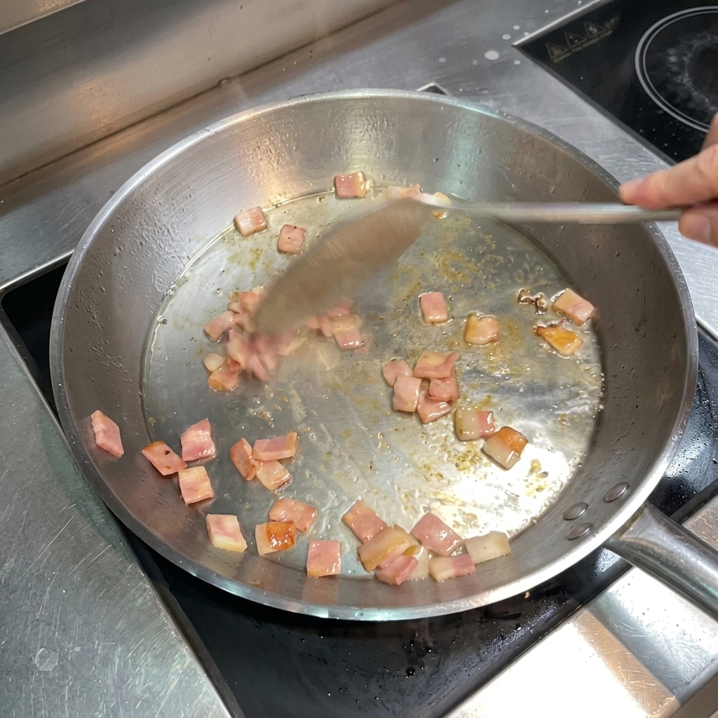 A metal spatula stirring browned, crispy diced bacon in a pan.