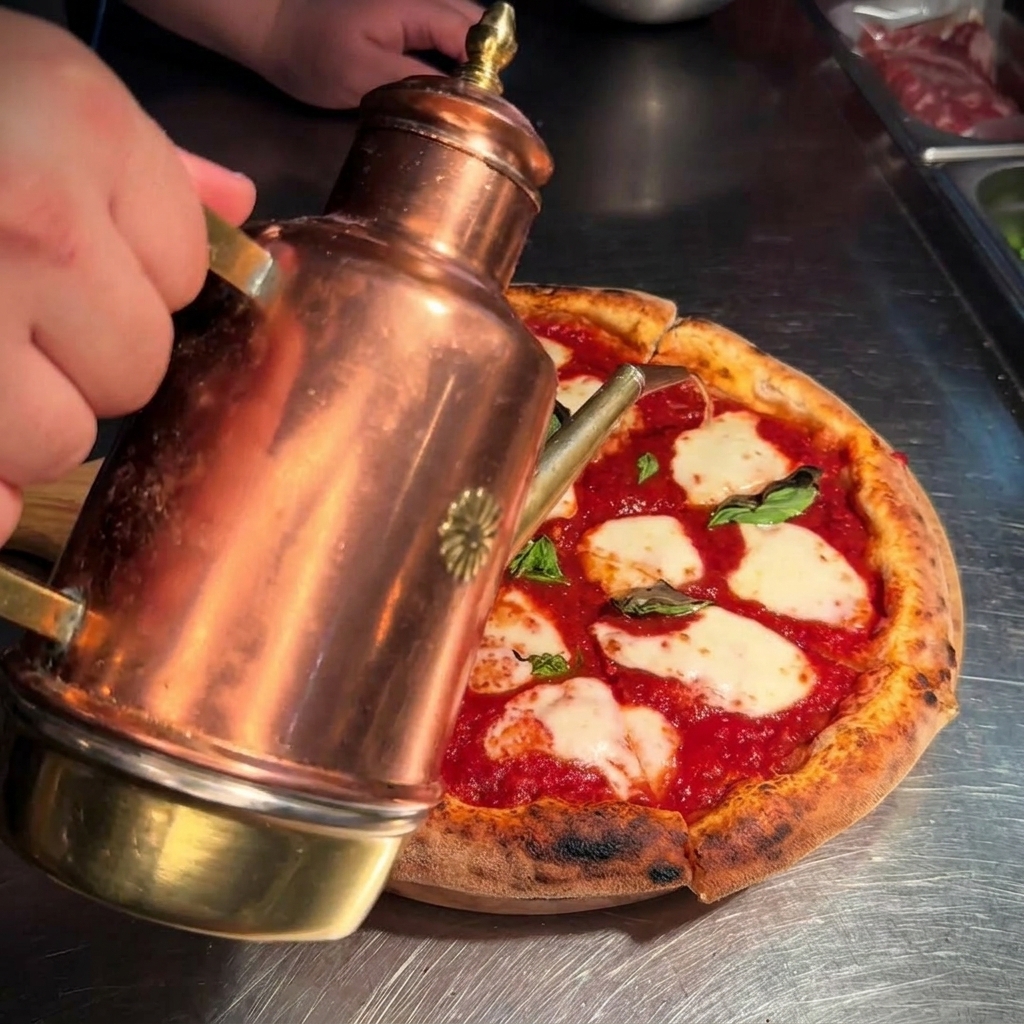 Golden olive oil being drizzled from a decorative copper can onto a hot, freshly sliced Margherita pizza.