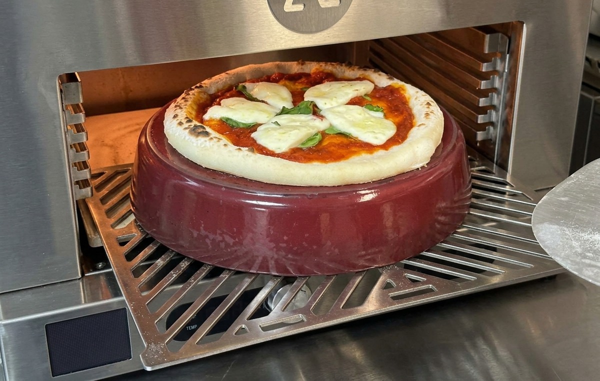 A partially baked pizza with melted mozzarella inside a hot oven, showing the crust beginning to puff and blister.