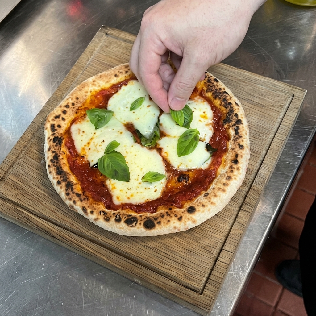 A hand placing vibrant green basil leaves onto a hot, freshly baked pizza with melted mozzarella and a blistered crust resting on a wooden board.