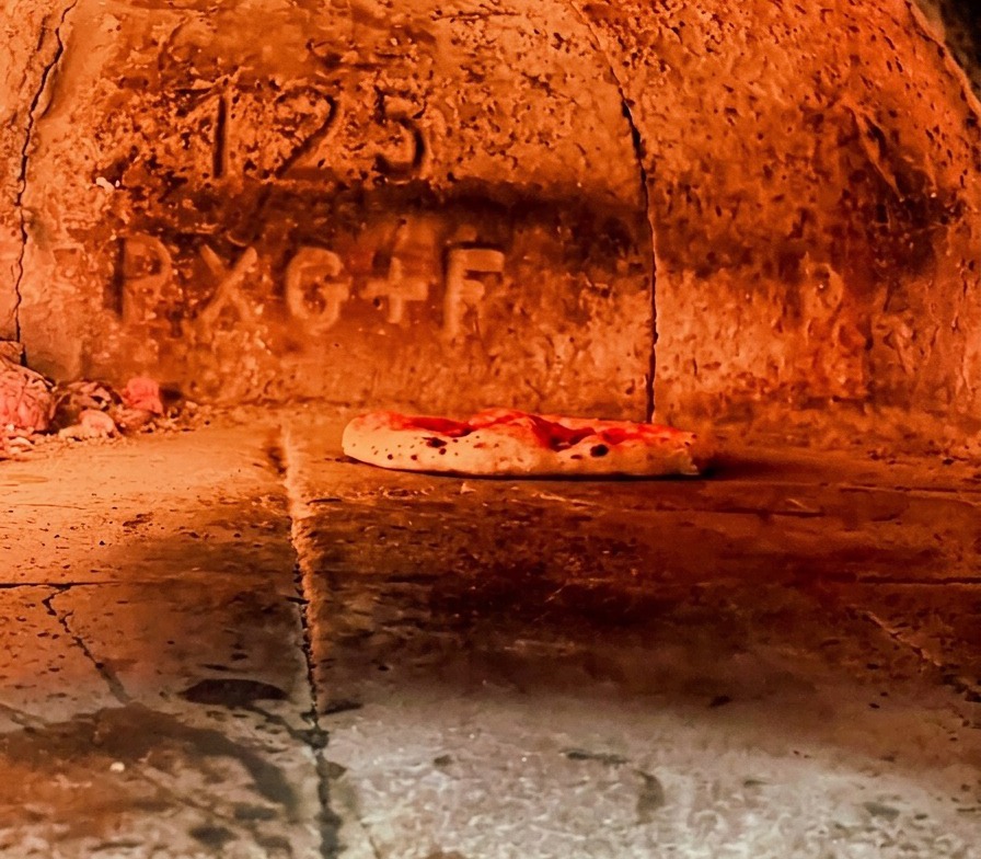 Neapolitan pizza baking inside a blazing hot wood fired oven with the crust starting to puff up.