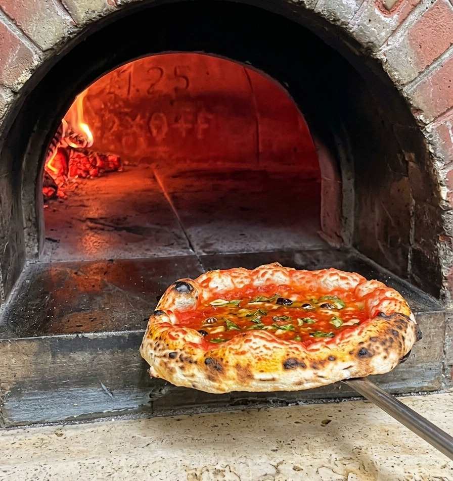 A freshly baked Neapolitan pizza with a blistered crust being pulled out of a wood fired oven on a metal peel.