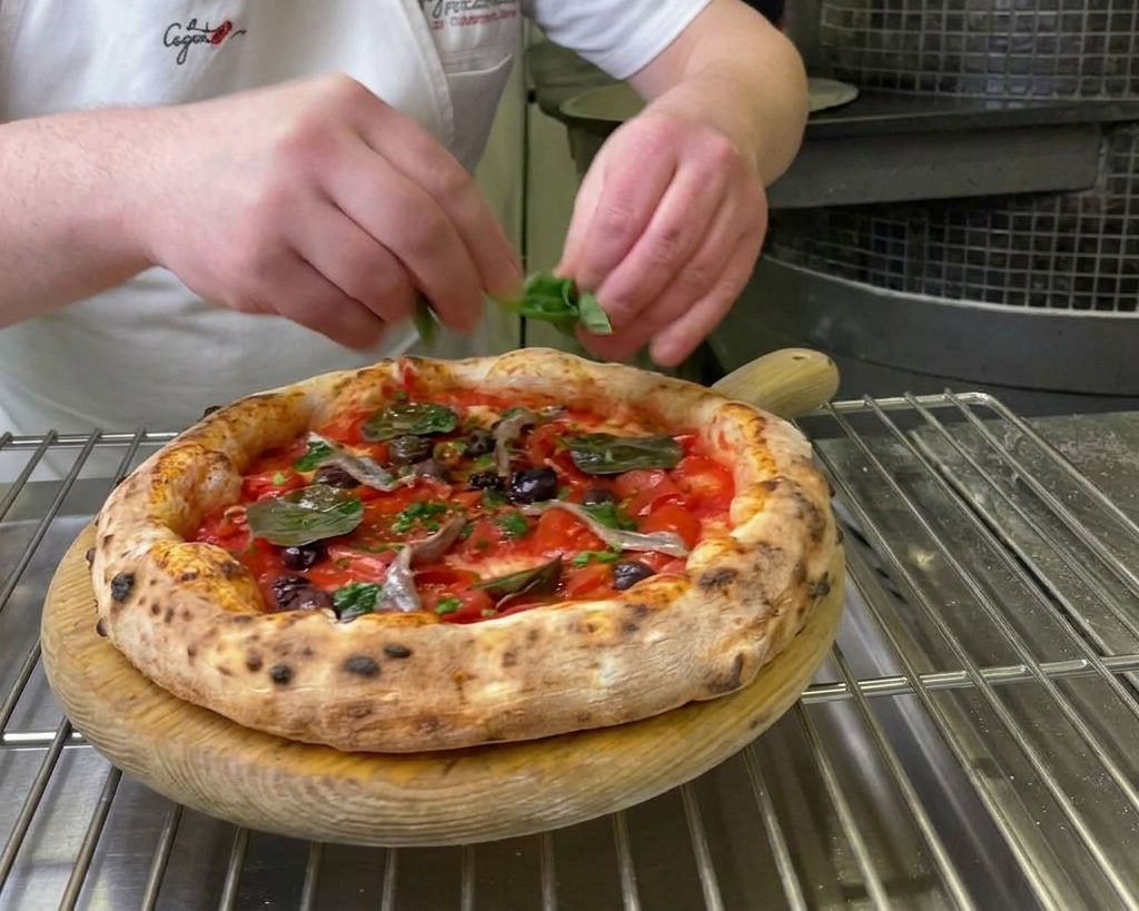 Chefs hands placing fresh green basil leaves onto a freshly baked Marinara pizza.