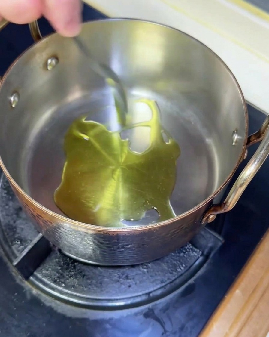 Olive oil shimmering as it heats up in a copper pot on a gas stove.