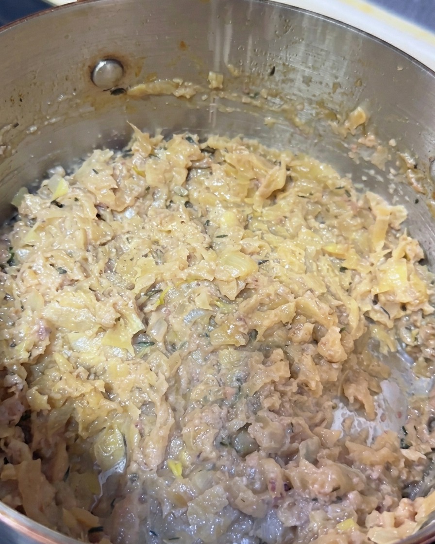 A close-up view inside a metal pot showing heavily caramelized onions combined with mashed fish paste and flecks of thyme.
