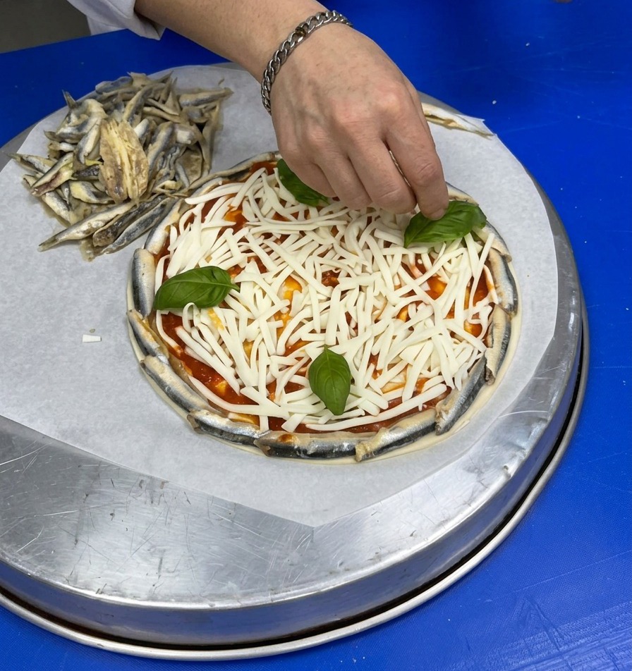 A hand placing fresh whole basil leaves on top of a bed of shredded white cheese on a pizza base.
