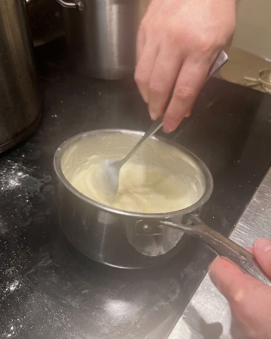 A creamy, thickened white sauce being stirred in a saucepan.