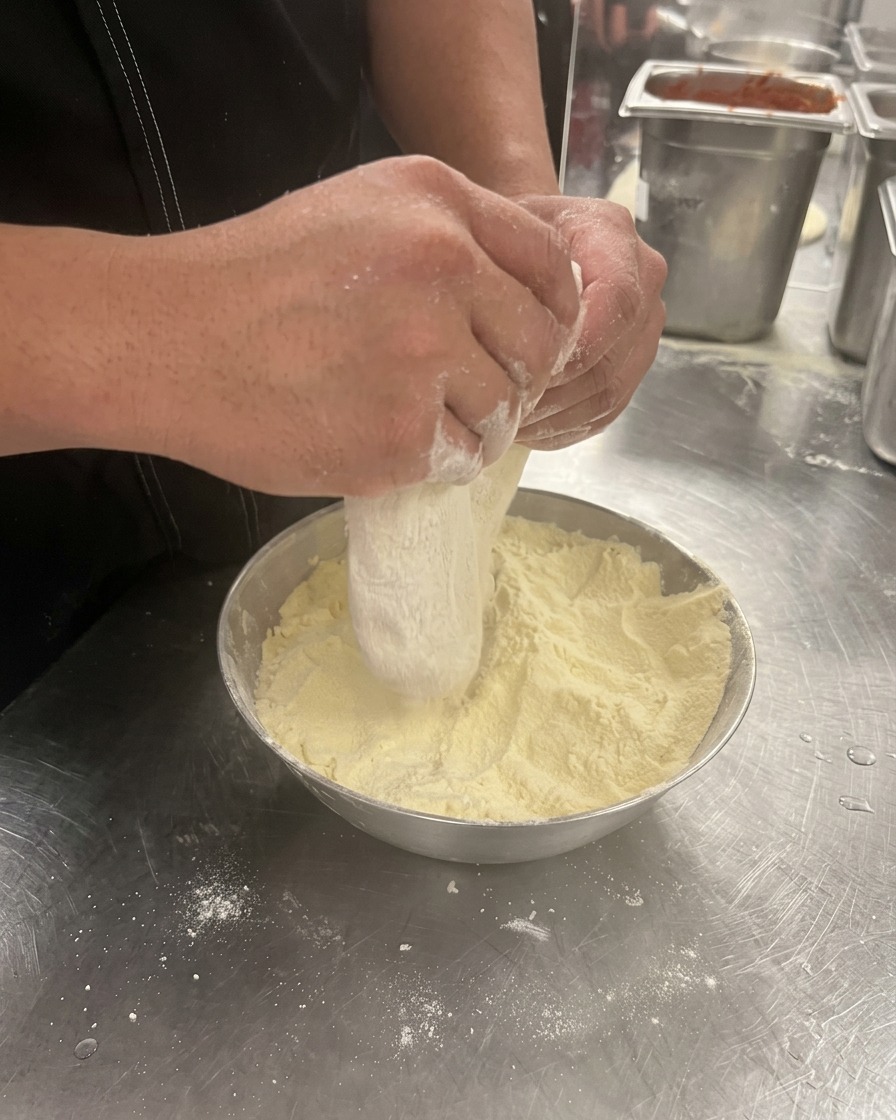 Hands pressing and stretching a ball of pizza dough in a bowl of flour.