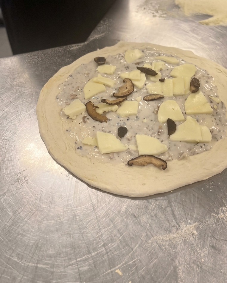 Scattering cooked slices of shiitake and button mushrooms over the mozzarella cheese on the raw pizza.