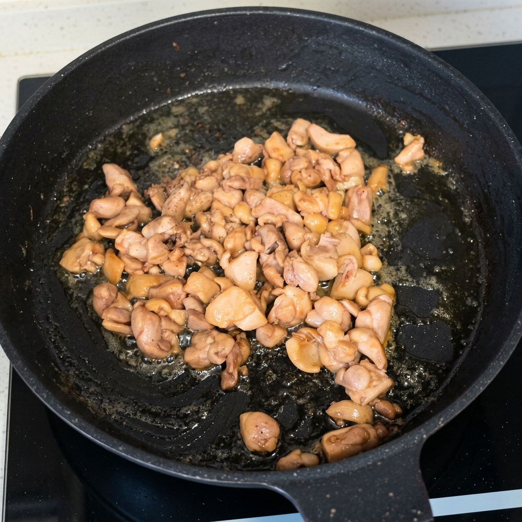 Cooked and browned chicken pieces being stir-fried in a black skillet.