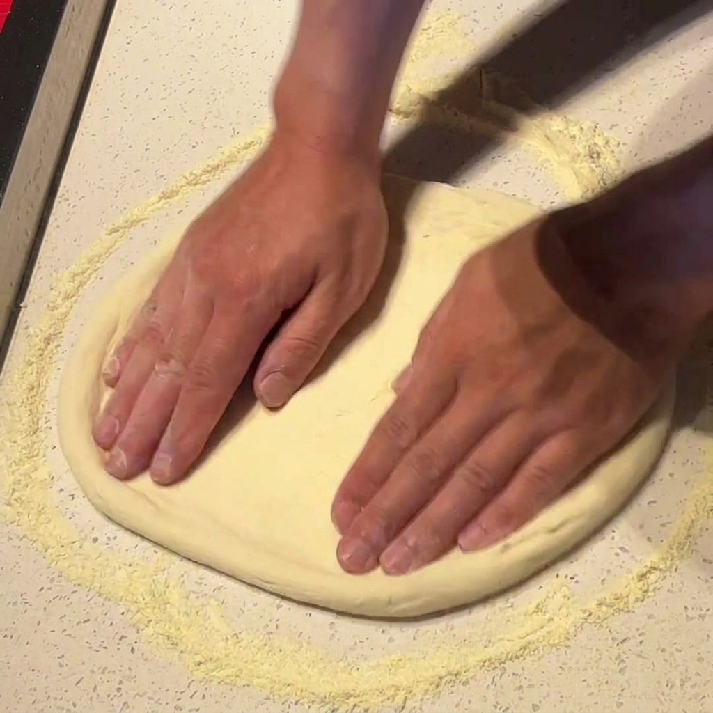 Hands pressing and stretching pizza dough wider on a floured surface.