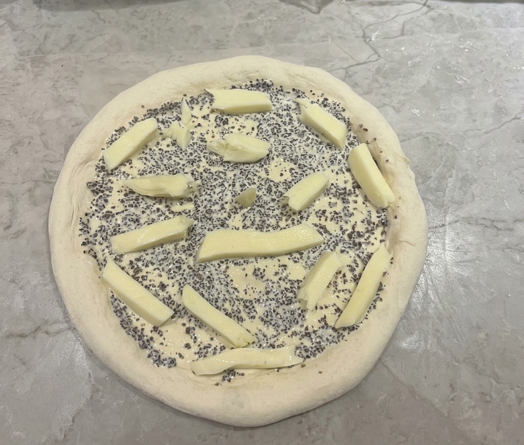 Pizza dough topped with black truffle sauce and scattered pieces of stick-shaped mozzarella cheese.