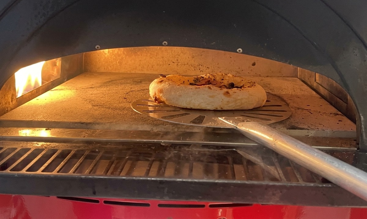 A small pizza with mushrooms and sausage baking inside a hot oven on a stone surface, with the crust visibly puffing up.