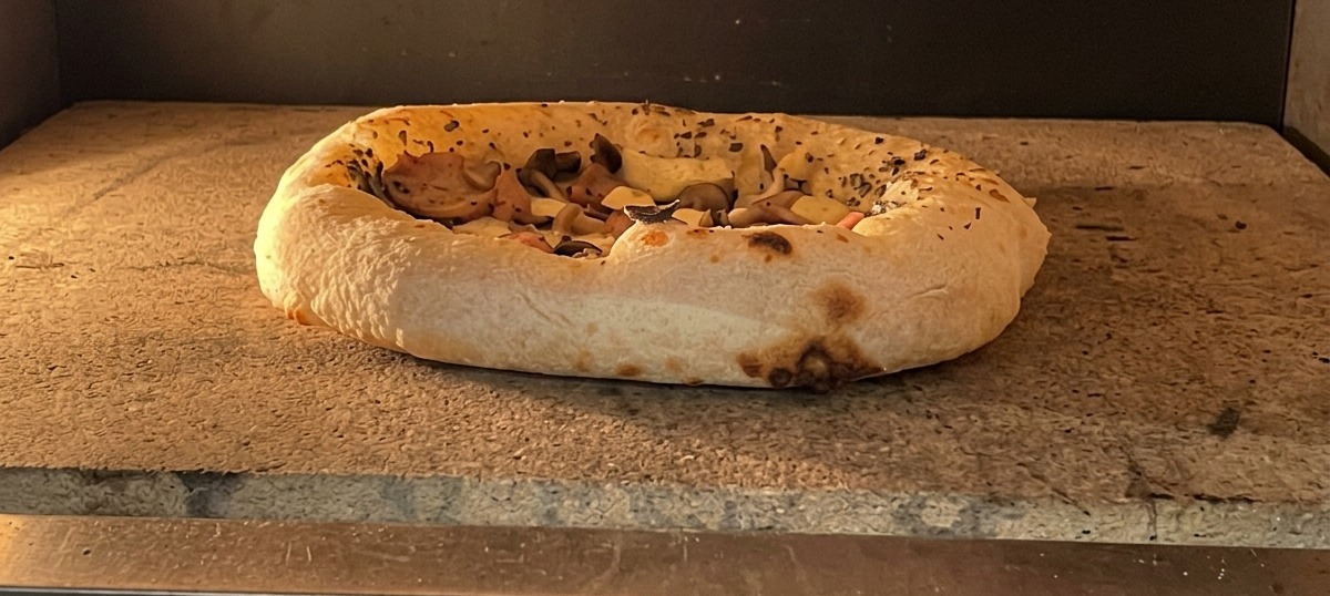 A pizza baking in the oven with the crust visibly puffed up and showing slight browning.