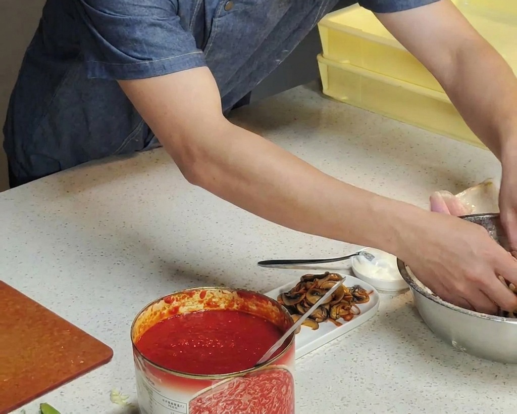 Chefs hands dipping a ball of fermented pizza dough into a silver bowl filled with dry white flour.