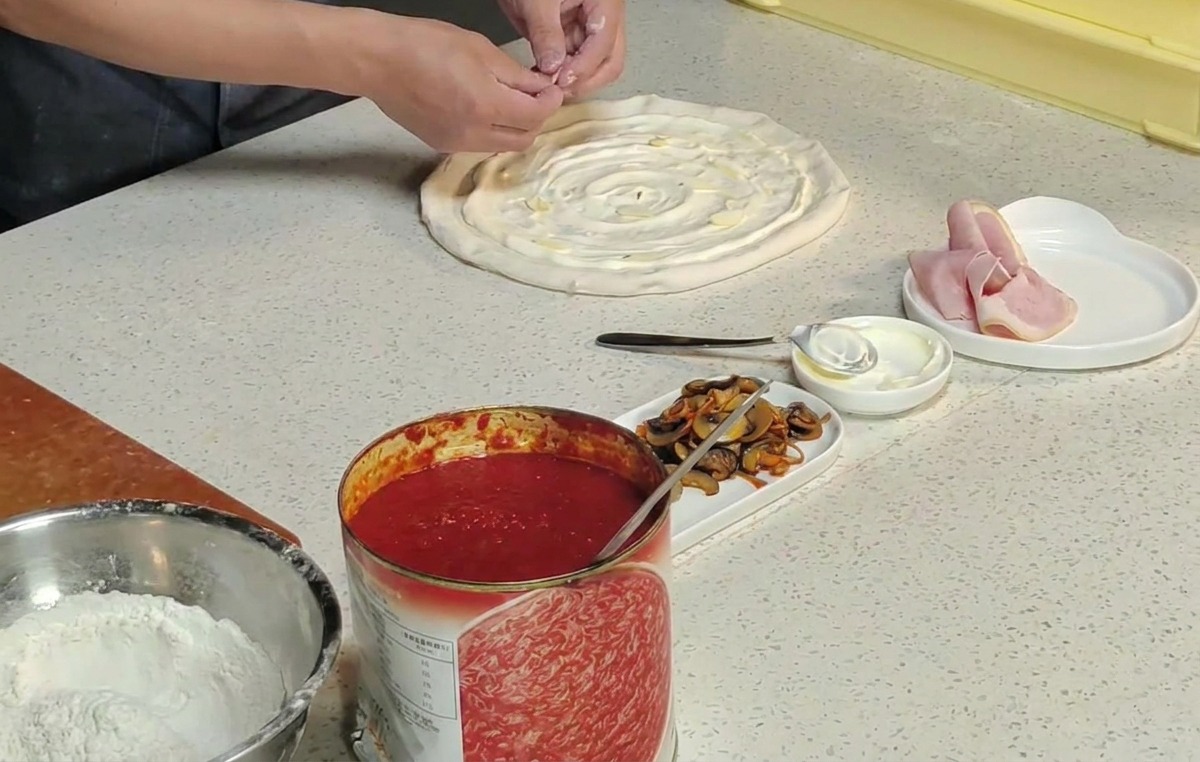 Chefs hands placing orange cordyceps flowers onto a raw pizza base coated with white sauce.