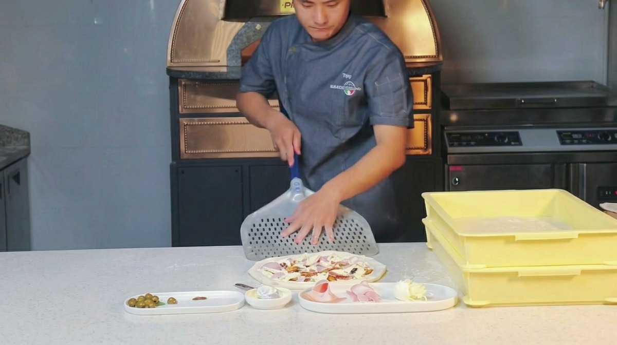 Chef rubbing dry flour onto a perforated metal pizza peel.