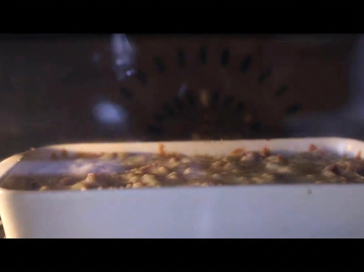 A close-up view of the baking dish inside a hot oven, with the cheese layer visibly bubbling and melting.