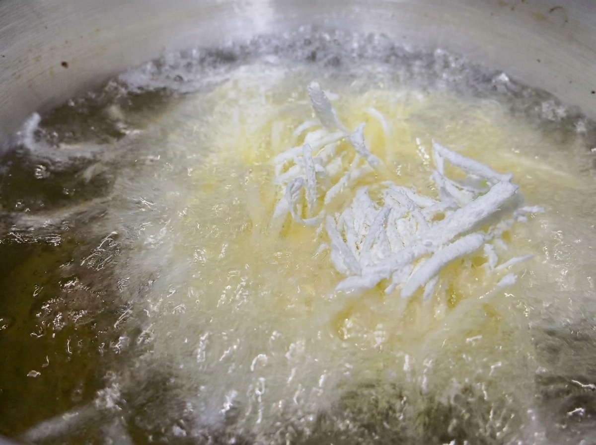Flour-coated potato shreds deep-frying in a pot of bubbling hot oil.