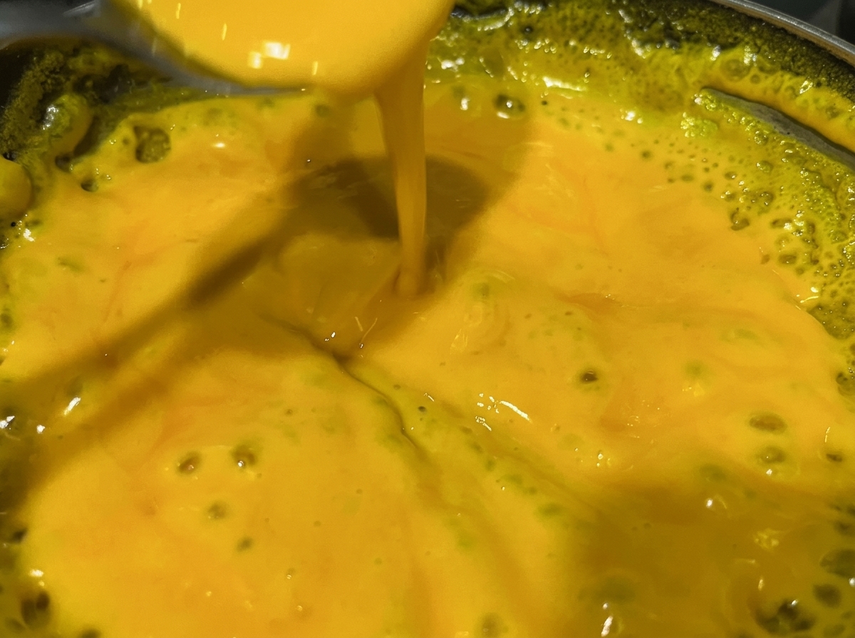 A spoon stirring a bright yellow, bubbling cheese sauce in a metallic pan.