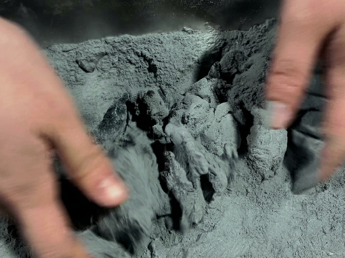 Hands vigorously rubbing marinated chicken pieces in a dark grey powder mixture inside a container.