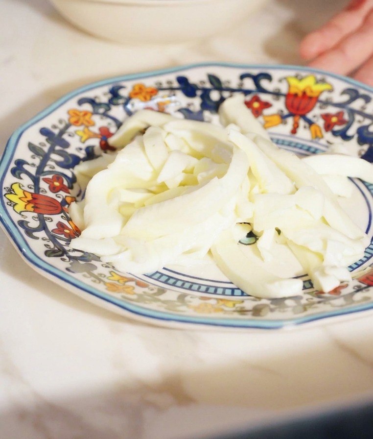 Small, uniform strips of white fior di latte cheese piled on a small decorative plate.