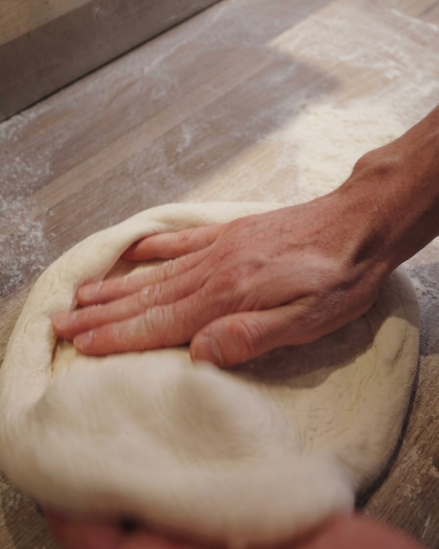 Hands gently pressing and stretching a round piece of pizza dough on a floured surface.