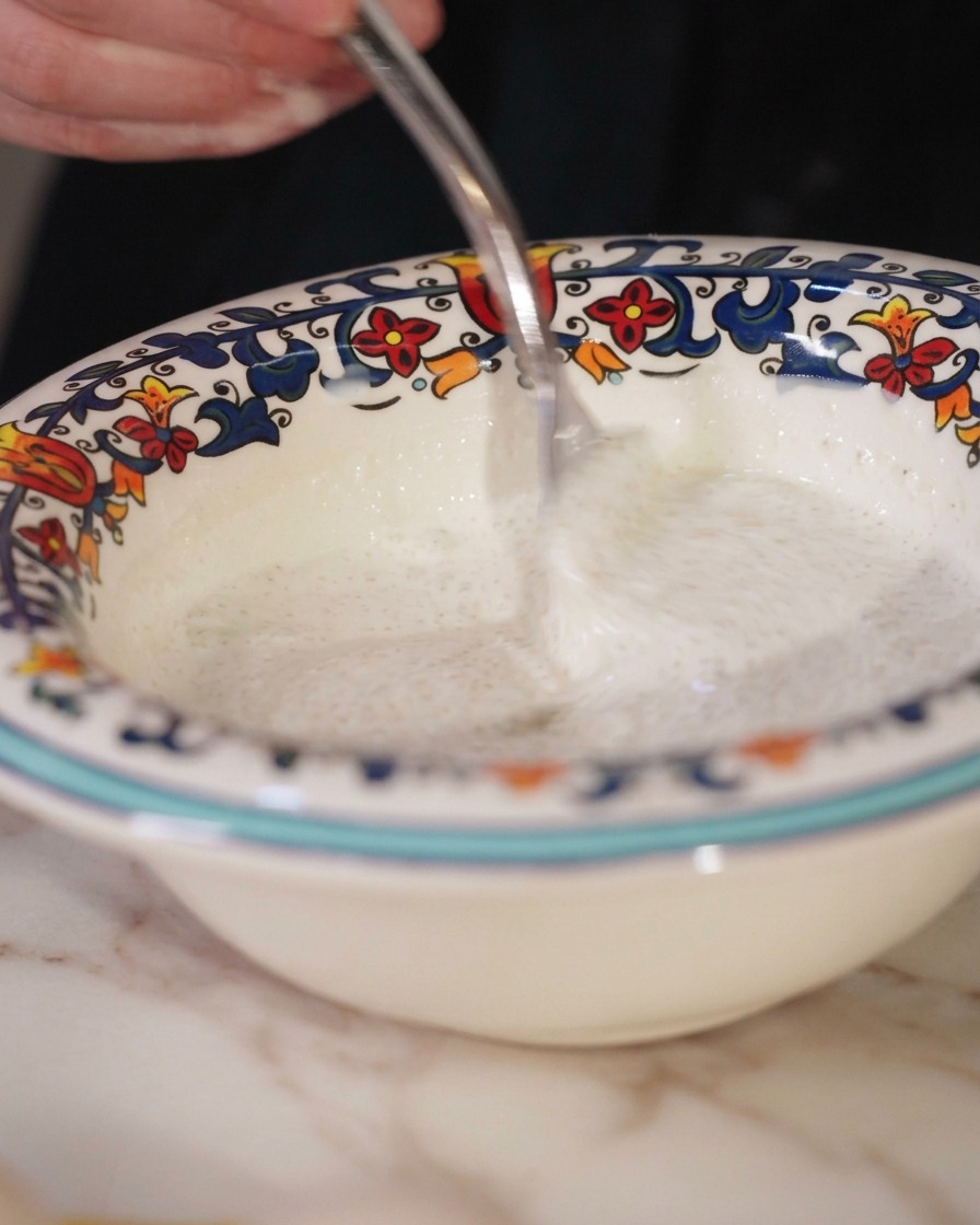 Stirring a mixture of cream and truffle paste in a decorative bowl with a fork.