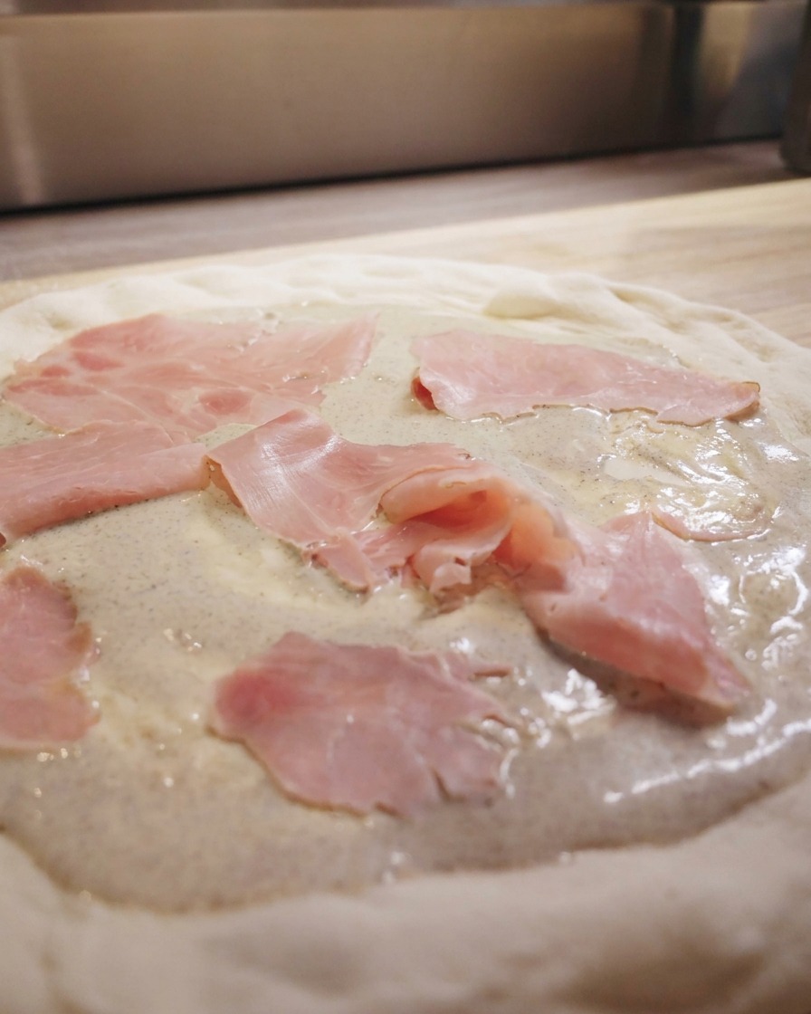 Slices of pink ham scattered over a pizza crust spread with creamy black truffle sauce.
