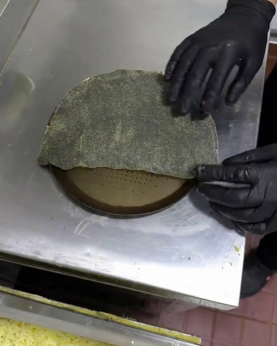 Gloved hands folding black dough over to form a half-moon shaped calzone.