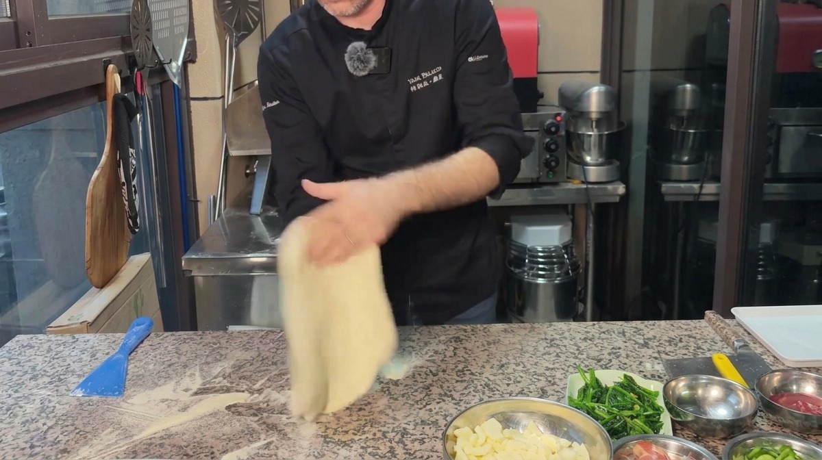 Chef stretching pizza dough into a circle on a floured marble surface.