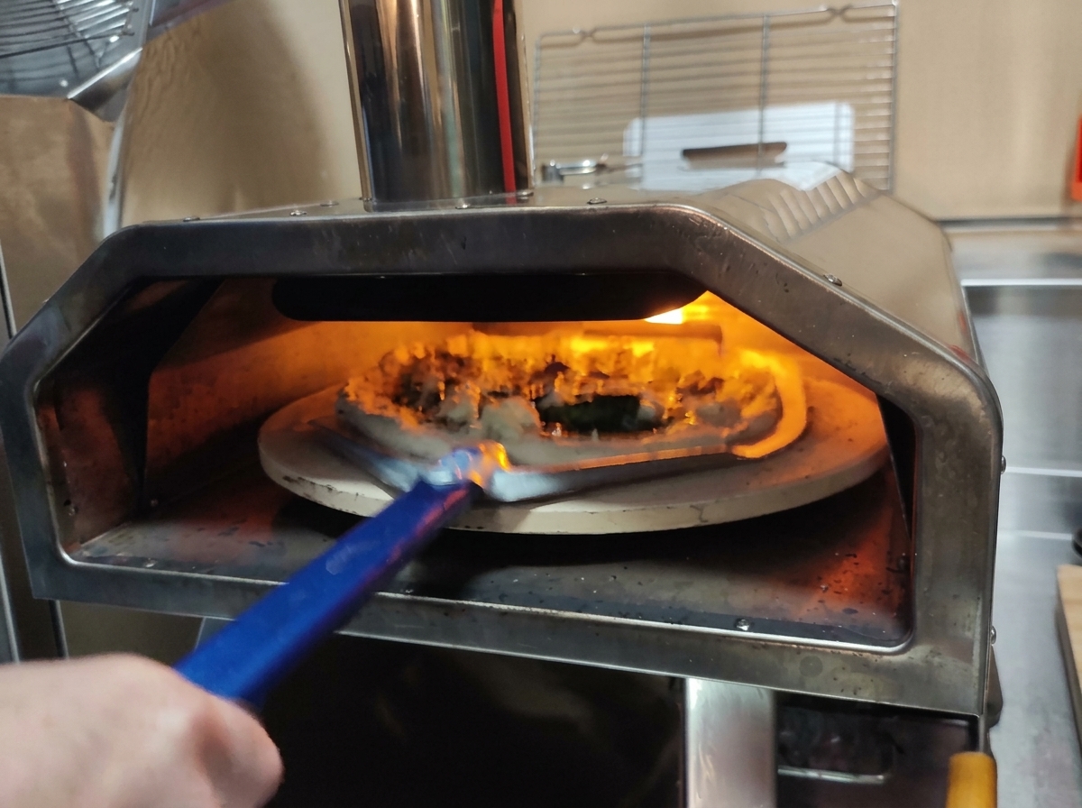 Using a perforated metal pizza peel to lift a raw pizza into a fiery oven.